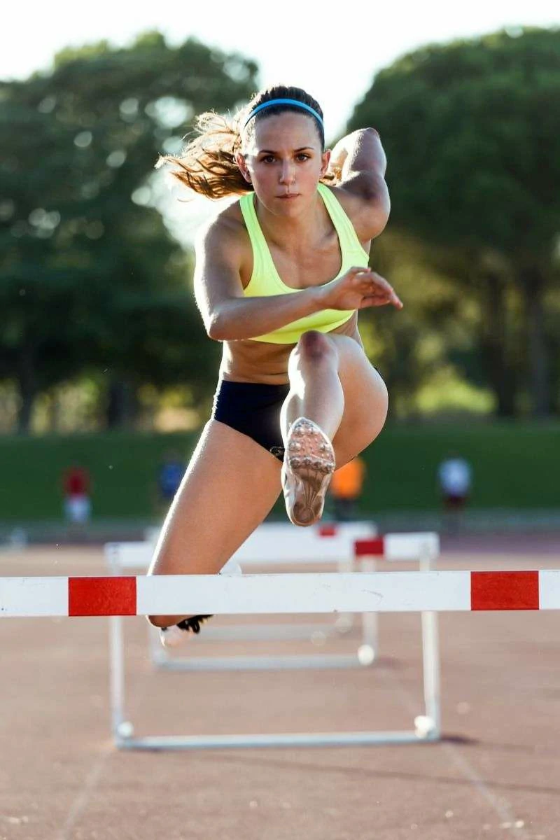 This image captures a woman mid-leap over a hurdle, her body and mind working in serious, perfect sync to overcome the obstacle.