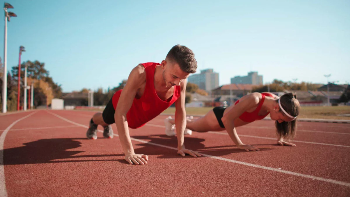 This image shows a manand woman doing push-ups on a running field, illustrating the focus and determination required to improve their physical and mental strength.