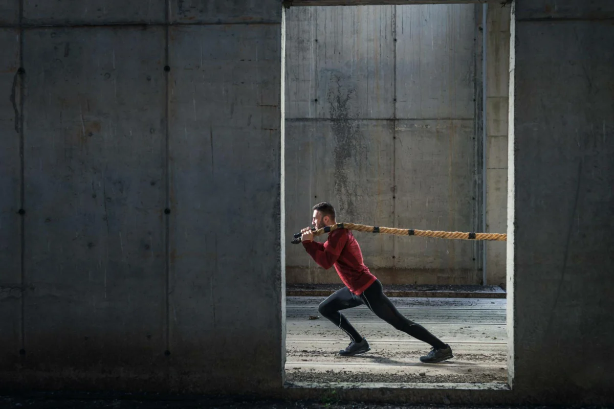 This image shows a man holding a large rope and pulling a tied object, illustrating the physical and mental effort required to overcome significant challenges.