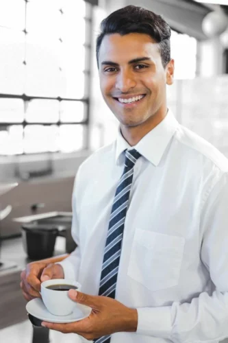A man in a business suit is smiling as he holds a cup of coffee. His posture is confident and relaxed, suggesting he is mentally prepared and focused