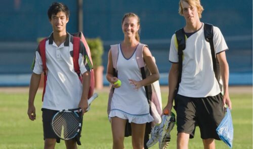 1. Smiling student-athletes carrying tennis gear, reflecting teamwork and positive mental health of student-athletes.