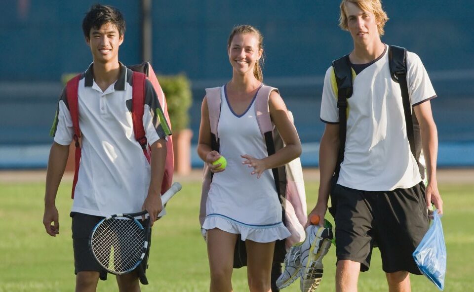 1. Smiling student-athletes carrying tennis gear, reflecting teamwork and positive mental health of student-athletes.