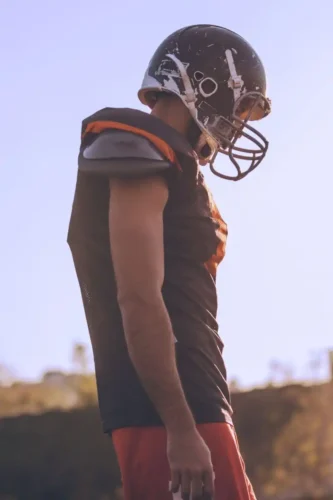 This image shows an NFL player in full practice gear standing amidst training equipment, representing the intersection of physical readiness and the psychological endurance needed for a full season.