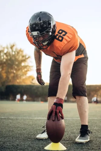 This image features a professional NFL athlete in a low stance, meticulously setting the football on the turf, with every muscle primed for explosive movement.